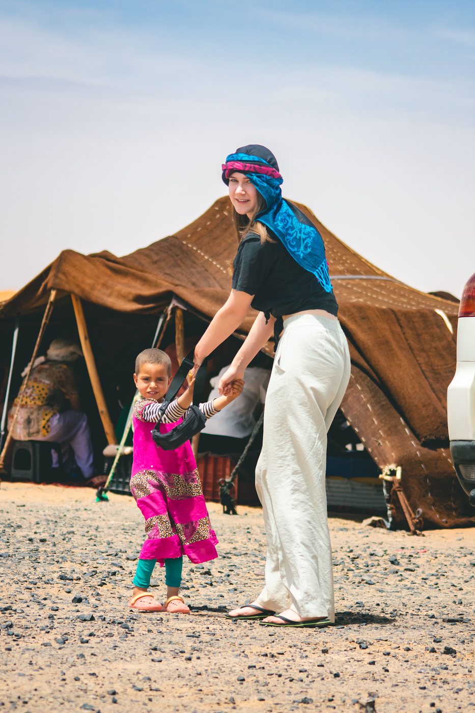 A smiling woman and child holding hands at a desert camp in Merzouga